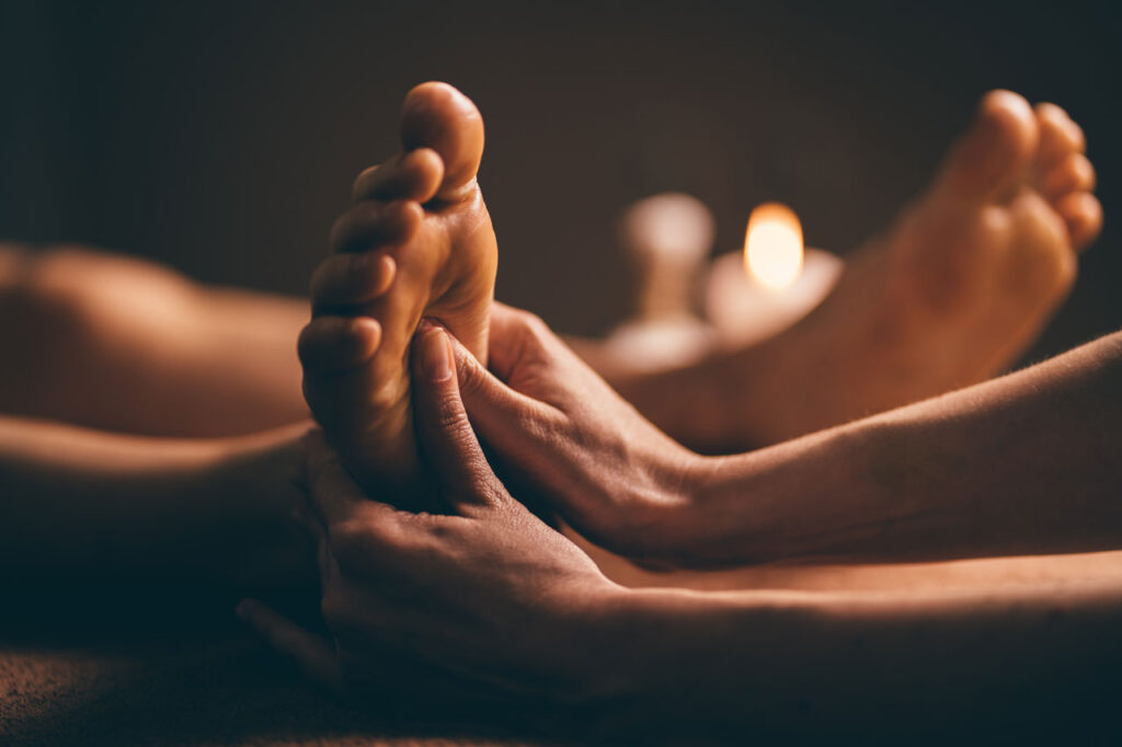 Person receives relaxing foot massage in candlelit room.